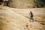 Elevated rear view of young man mountain biking on dirt track, Mount Diablo, Bay Area, California, USA