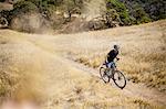 Elevated view of young man mountain biking up dirt track, Mount Diablo, Bay Area, California, USA