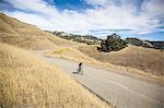 Elevated view of young man mountain biking up rural road, Mount Diablo, Bay Area, California, USA