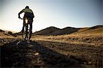 Silhouetted surface view of young man mountain biking up dirt track, Mount Diablo, Bay Area, California, USA