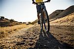 Silhouetted cropped view of young man mountain biking down dirt track, Mount Diablo, Bay Area, California, USA
