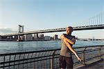 Young male runner stretching in front of Manhattan bridge, New York, USA