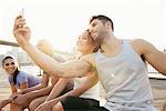 Young adult running couple taking smartphone selfie  on riverside, New York, USA