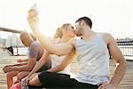 Young adult running couple kissing for smartphone selfie  on riverside, New York, USA