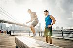 Personal trainer and young man training on riverside bench, Brooklyn, New York, USA