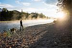 Woman walking dog on bank of Bitterroot River, Missoula, Montana, USA
