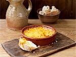Bowl of smoked cheese bake, crusty bread on wooden chopping board