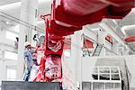 Male factory worker spray painting a crane arm red in factory workshop, China