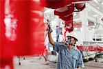 Male factory worker spray painting a red crane in factory workshop, China