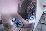 Two male welders working in industrial pipe at crane factory, China