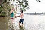 Young couple rope swinging above lake