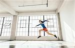 Side view of young woman in gym doing powerful mid air running stance