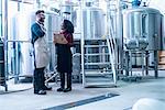 Colleagues in brewery holding clipboard face to face smiling