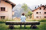 Rear view of boy sitting log bench looking away at view of mountains