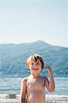 Bare chested boy on beach and mountain range looking at camera smiling, Luino, Lombardy, Italy