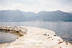 Stone pier curving through water by mountain range, Luino, Lombardy, Italy