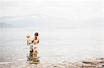 Rear view of mother standing in lake holding boy looking away at view of mountain range, Luino, Lombardy, Italy