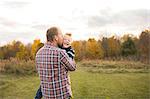 Rear view of father carrying smiling son, kissing him on cheek