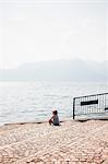 Rear view of boy sitting cobbled steps looking out at view, Luino, Lombardy, Italy