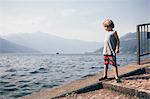 Boy standing on slope by water looking away, Luino, Lombardy, Italy