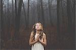 Portrait of long blond haired girl with eyes closed and hands together in misty forest