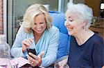 Two women, sitting outdoors, looking at smartphone