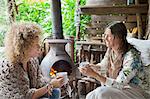 Two female friends drinking coffee in open cabin with wood stove