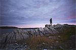 Hiker hiking on rocks at dusk, Fogo Island, Newfoundland, Canada