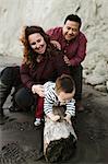 Family with baby boy sitting on driftwood on beach