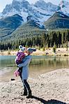 Mother holding and kissing daughter beside river, Three Sisters, Rocky Mountains, Canmore, Alberta, Canada