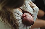 Over shoulder view of mid adult woman cradling new born baby daughter wrapped in cardigan