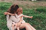 Girl sitting on mother's lap on windy field