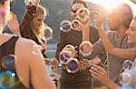 Adult friends playing with floating bubbles at roof terrace party