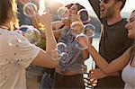 Adult friends playing with floating bubbles at roof terrace party