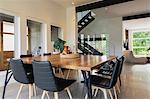 American walnut wood dining table and black leather sitting chairs with ash wood legs in the dining room inside a modern cube style home, Quebec, Canada