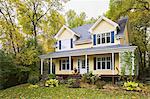 Yellow clapboard with blue and white trim cottage style home facade in autumn, Quebec, Canada