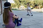 Teenage girl watching sister skateboarding on sidewalk