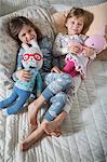 Sisters hugging soft toys on bed