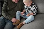 Father and son sitting on sofa, son looking at smartphone