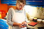 Senior woman in kitchen, using smartphone