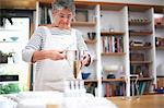 Senior woman using pancake funnel to pour mixture into plastic pots