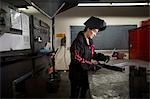 Female metalsmith examining metal rod at workshop bench