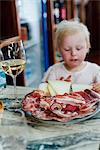 Plate with sliced hams and sausages and small girl in background