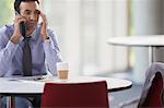 Stressed businessman talking on cell phone at table