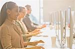 Smiling female telemarketer wearing headset talking on telephone at computer in sunny office