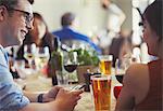 Couple with cell phone talking and drinking beer and wine at restaurant table