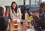 Friends clapping for happy woman with fireworks birthday cake at restaurant table