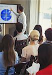 Business people in audience watching businessman leading conference presentation at television screen