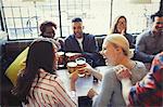 Laughing friends toasting beer glasses at table in bar