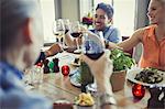 Smiling friends celebrating, toasting wine glasses at restaurant table